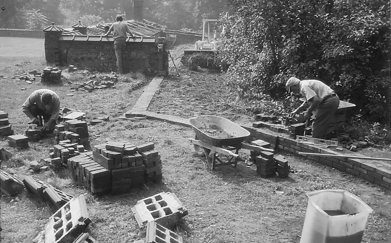 Three men laying brick walls in a garden.
