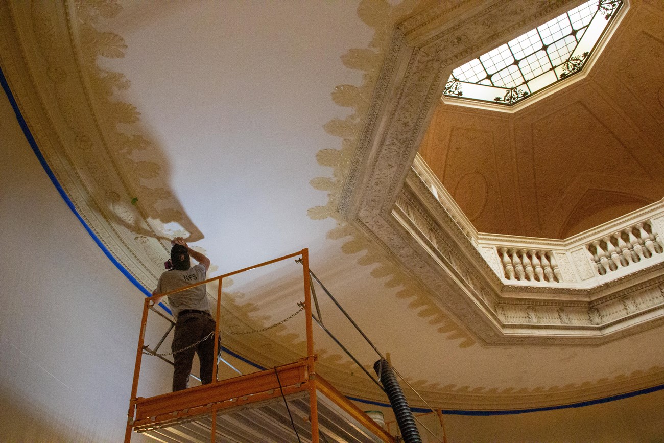 A man on scaffolding sanding an interior decorative ceiling.