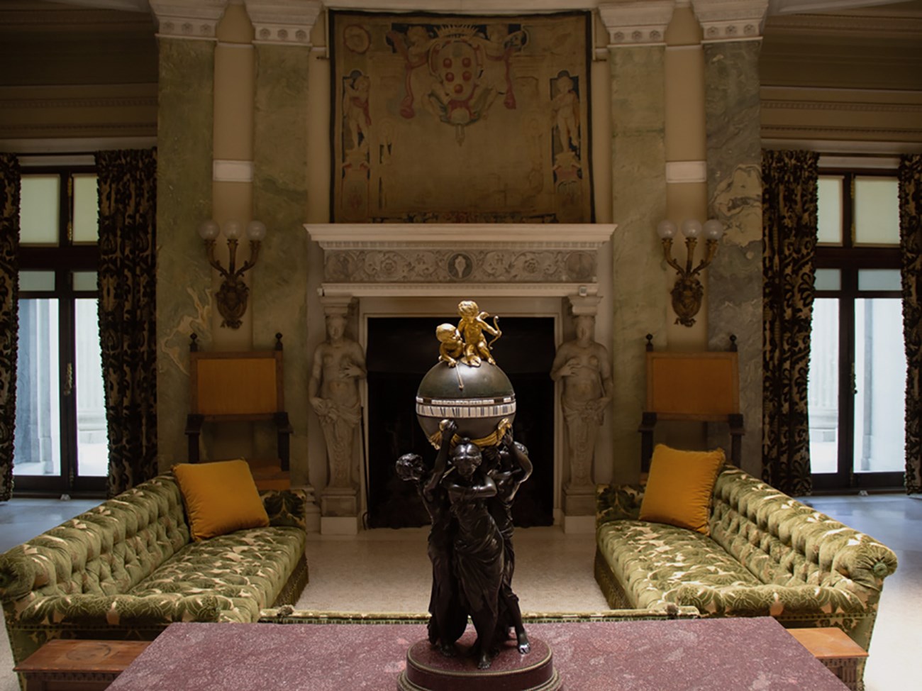 A grand room with central fireplace, tapestries, and sofas.