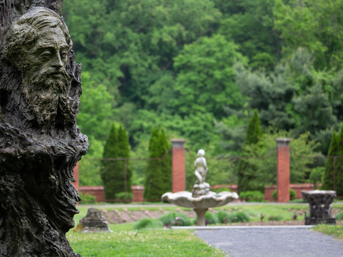 A bronze sculpture of a man's face set within a formal garden.