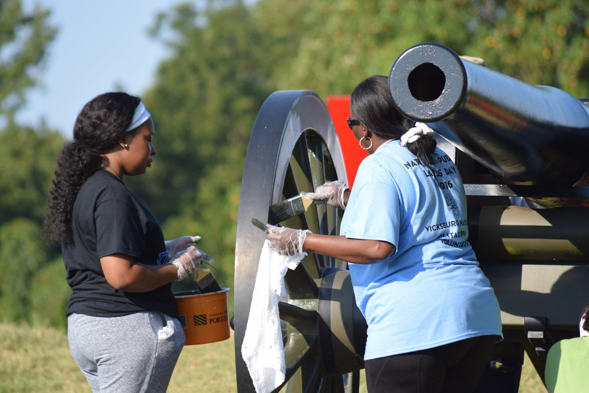 Two women cleaning a sign in the military park.