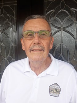 A white man in white polo shirt with gray hair, gray goatee, and glasses.