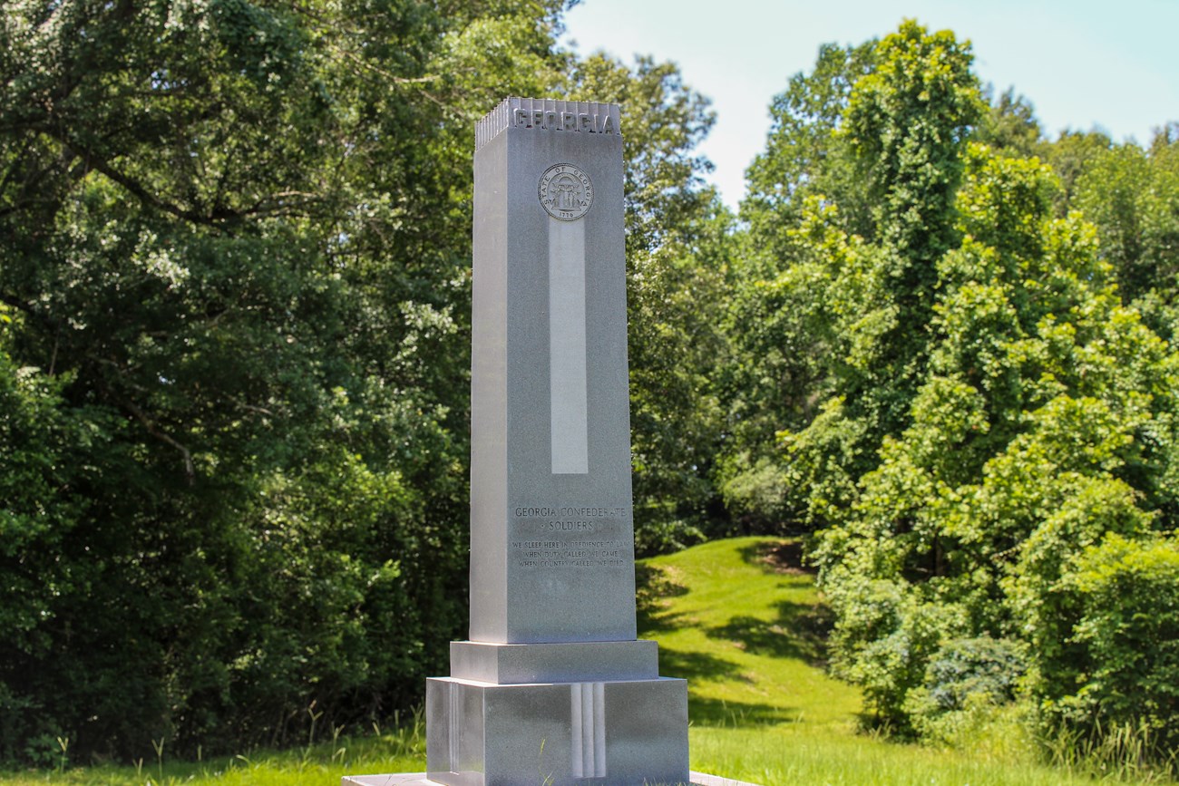 A large vertical monument that reads "Georgia" on top sits in a field surrounded by trees