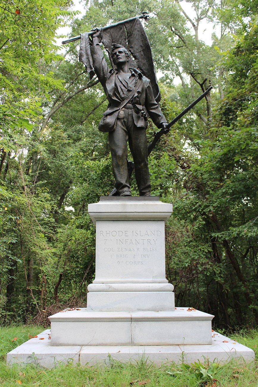 A bronze statue of a soldier holding the tattered American flag in one hand and a musket in the other hand.