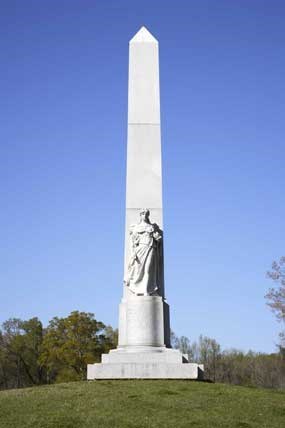 A tall white obelisk with statue of a woman on it