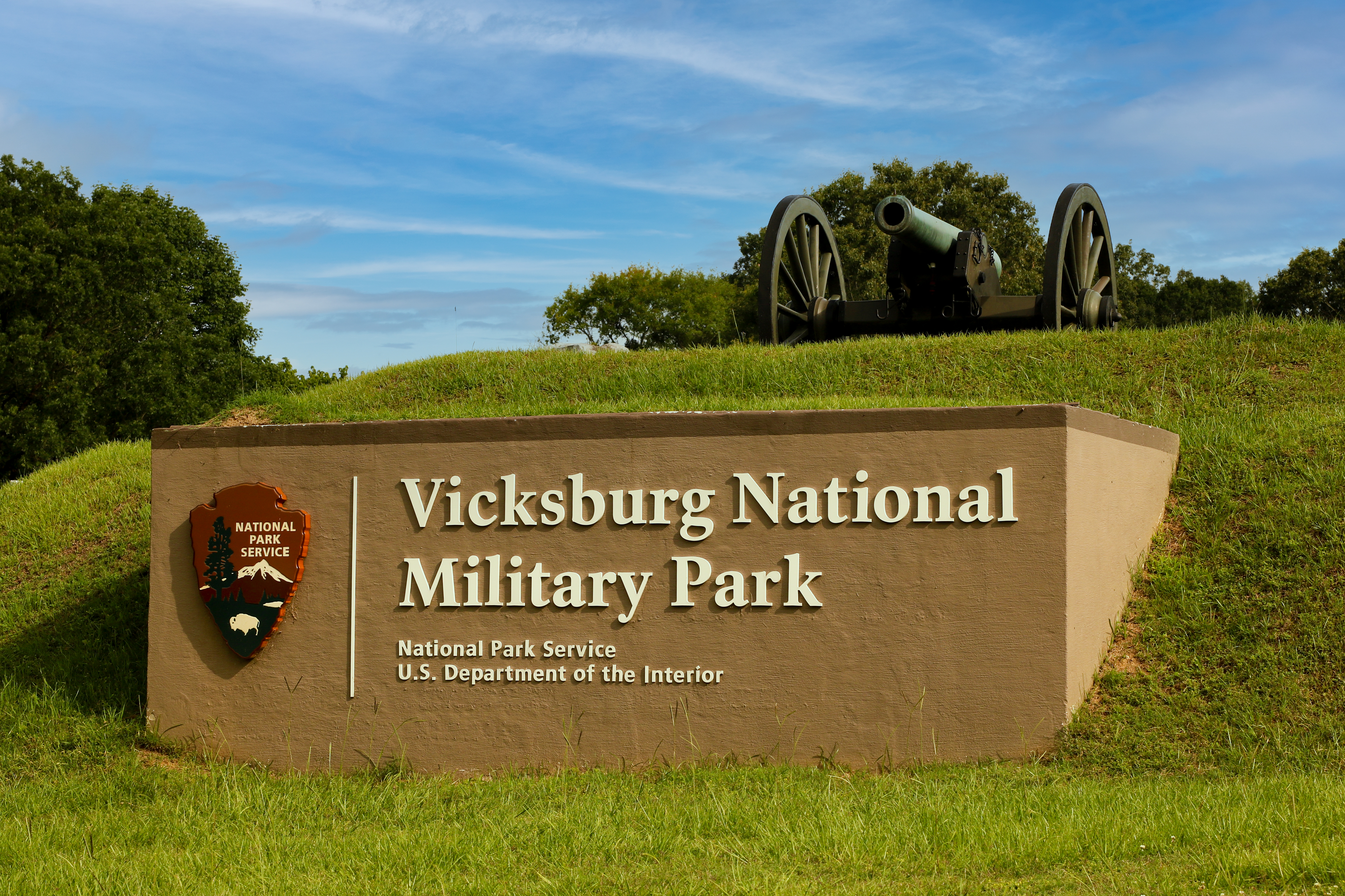 Vicksburg NMP ID Sign Grassy hill with cannon on top. Light brown cement sign in front with NPS Arrowhead and Vicksburg National Military Park