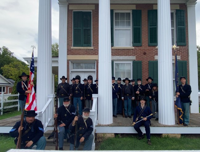 a group of reenactors in blue standing in front of a house.