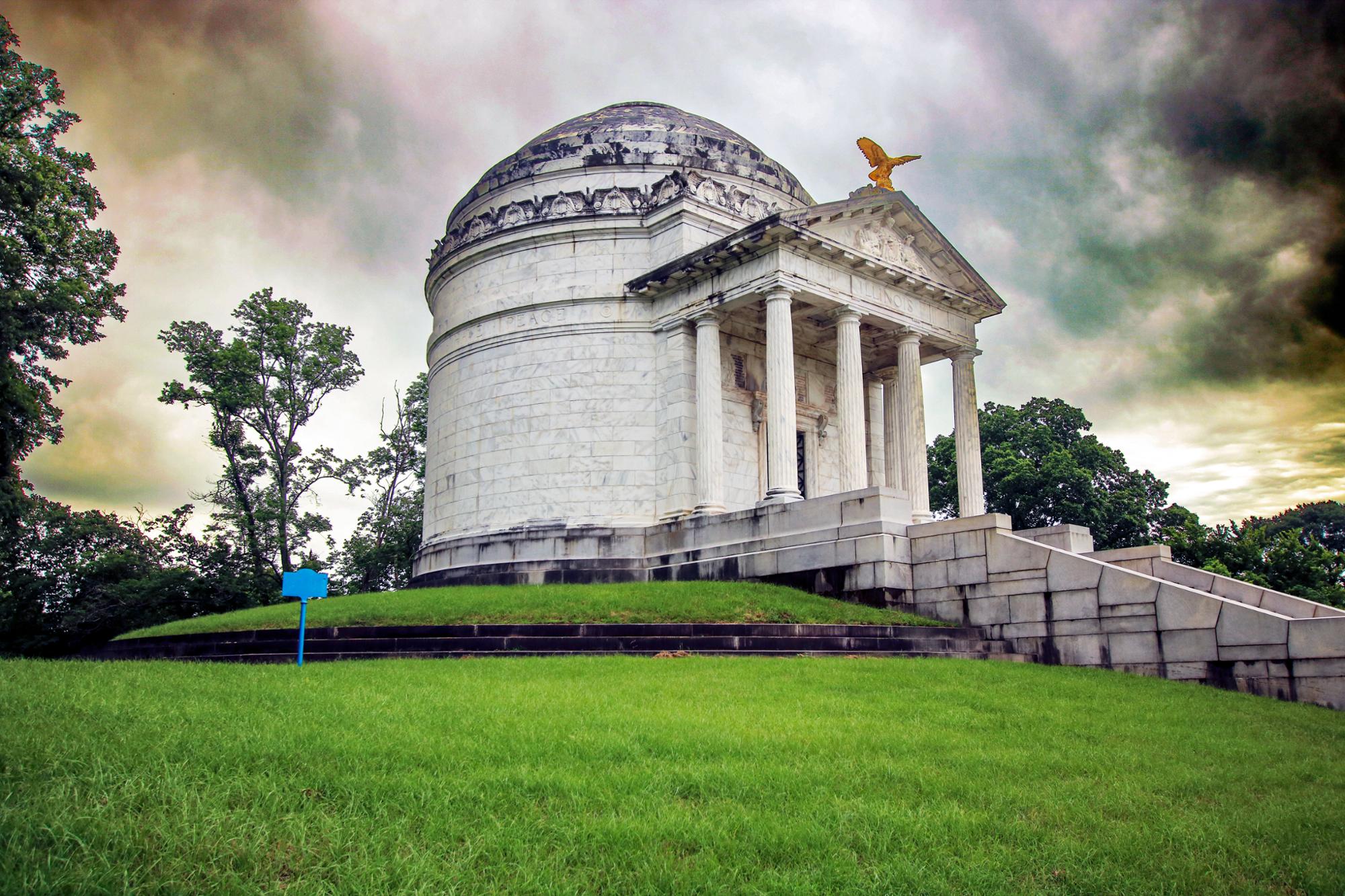 Illinois Memorial with storm clouds Large memorial stone structure with a domed roof and front pediment. Row of stone steps leading up to entrance. Dark clouds in sky above memorial.