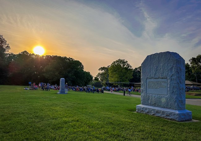 The sun set overs a crowd on the lawn in front of the park visitor center