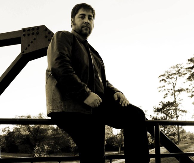 A man sitting on a railing looking at the camera.