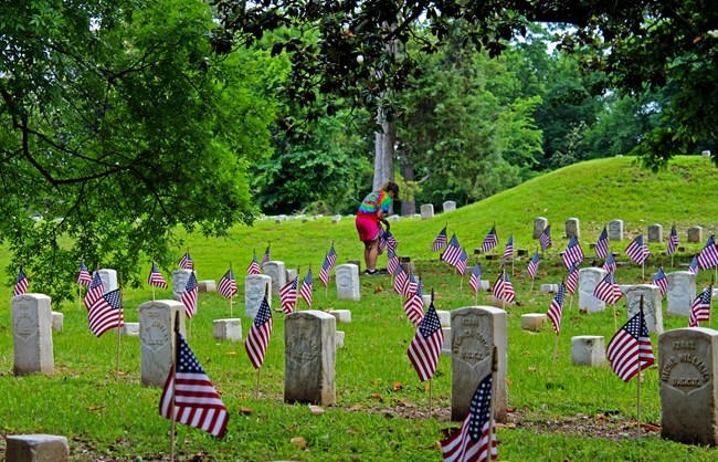 A woman places American Flags on several headstones