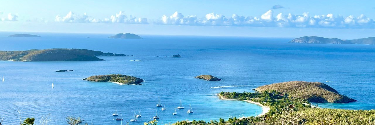 Image of a blue bay with white sand beach surrounded by green islands and sailboats.