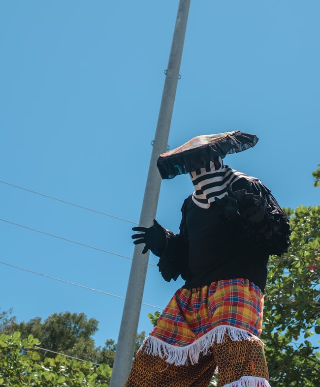 A Moko Jumbie stilt dancer in brilliantly colored ceremonial dress takes on a dramatic pose as he performs at Folk Life Festival on St. John.