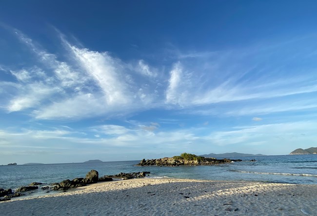 Clear blue water laps white sand beach sprinkled with rocks and coral.