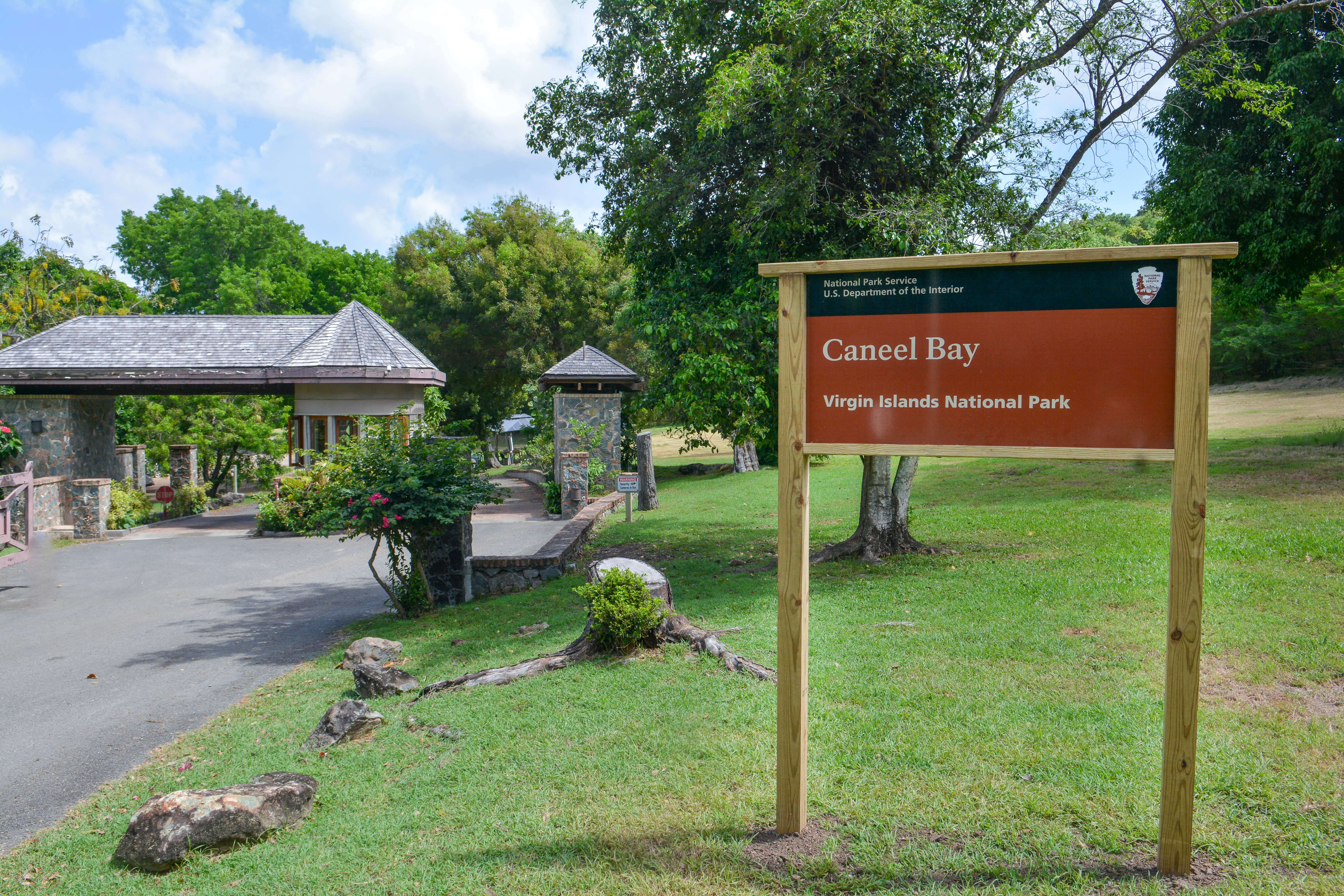 Caneel Bay Sign Image of a sign reading Caneel Bay in front of a driveway and small builing with green trees and blue sky.