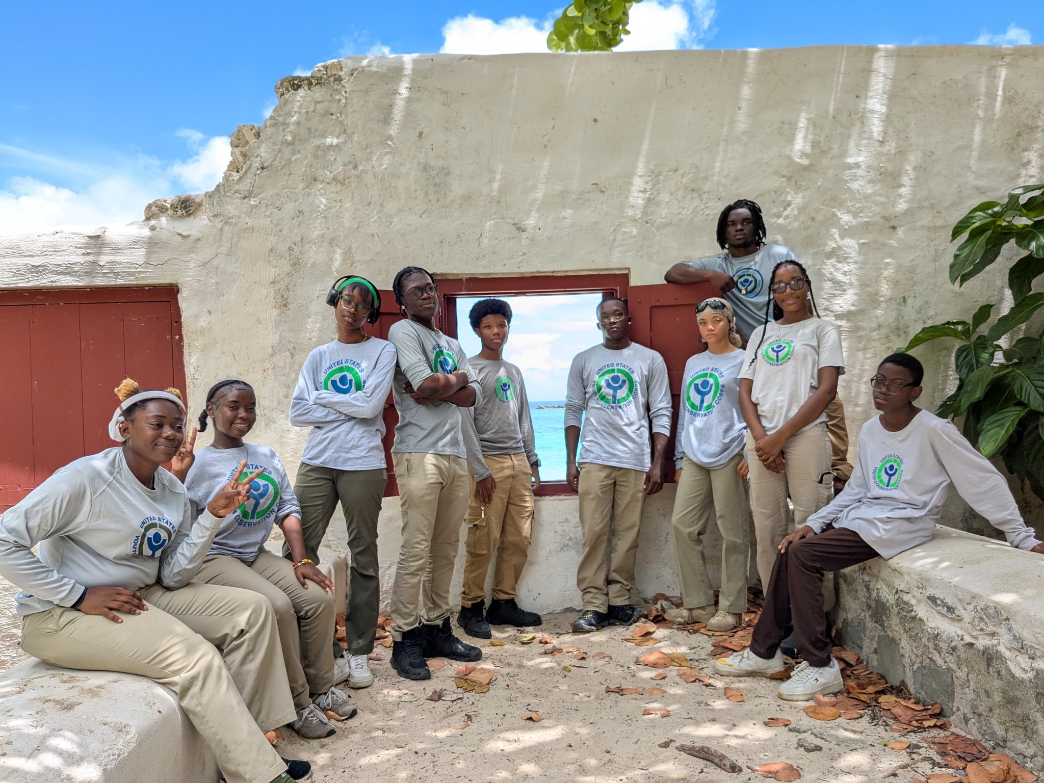 A group of about ten young people wearing matching gray shirts and khaki pants pose together outdoors