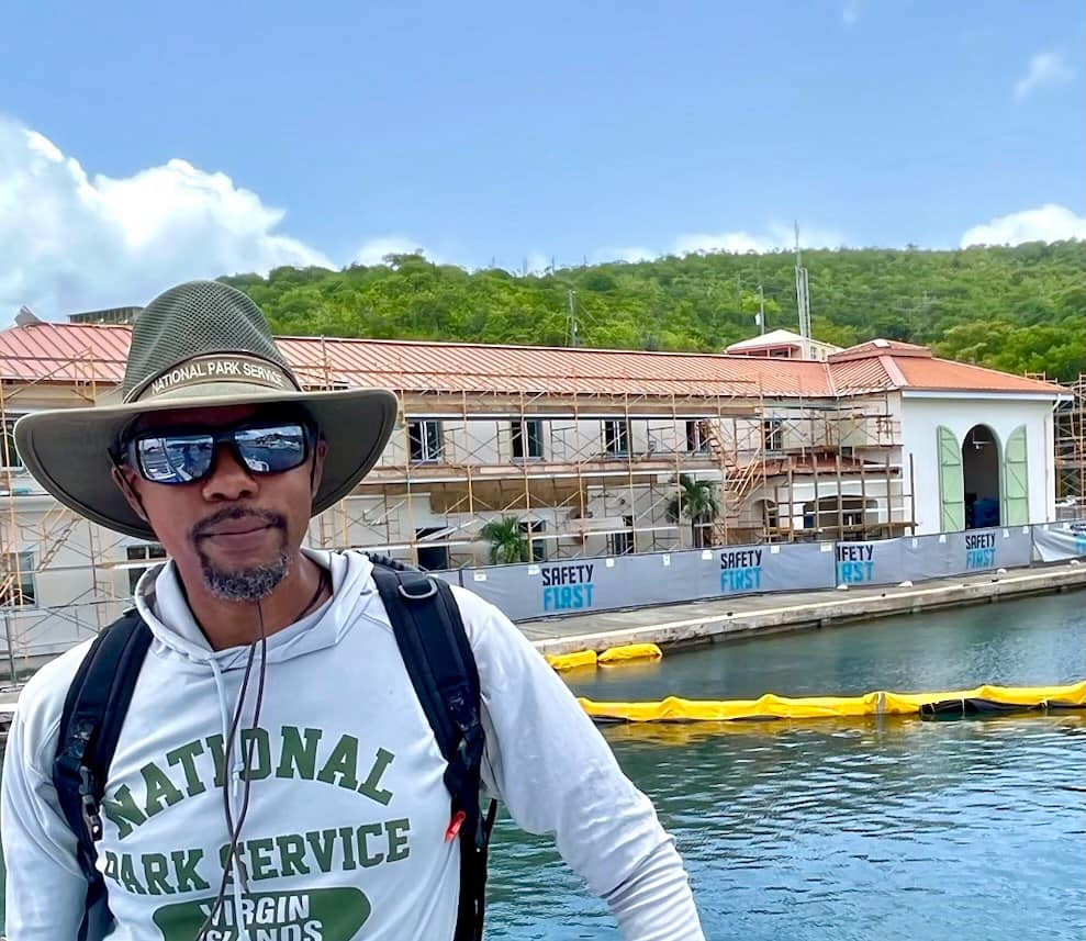 African American park superintendent stands in foreground with Virgin Islands National Park Visitor Center boat docks, building, and bulkhead under construction in background