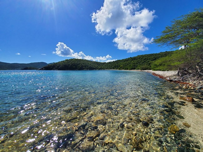 Haulover Bay's crystal clear waters stretch off to the left as the rolling green hills of Virgin Islands National Park are seen in the distance.