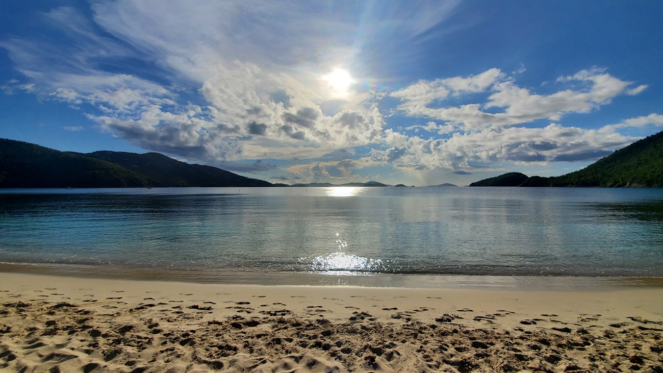 Framed by the green hillsides of St. John to the left and the right, the crystal clear blue water of Francis Bay stretches away from the white sand beach as the hangs in a blue sky smeared with puffy white clouds.