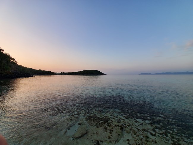 Beneath a clear blue sky, the calm, crystal clear water of Hawksnest Bay stretches off to the horizon with Turtle Point and the British Virgin Islands in the distance