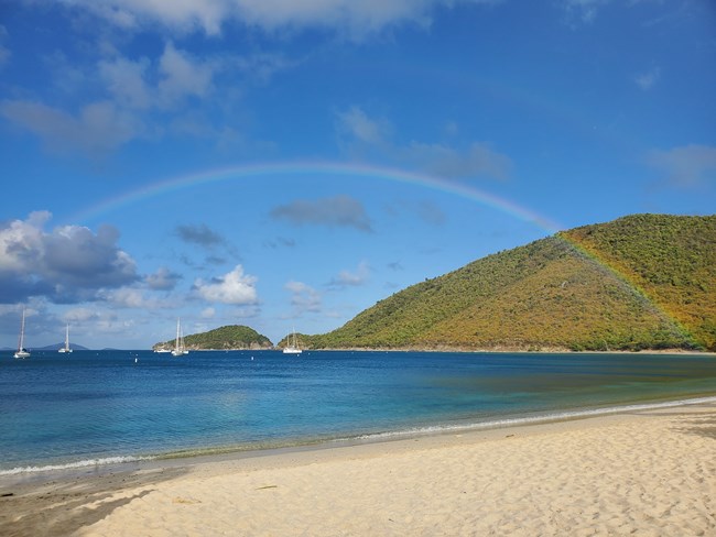 The white sand beach of Francis Bay is pictured its cool blue waters play host to a magnificent rainbow that stretches out over the green hillsides of Mary's Point and Whistling Cay.