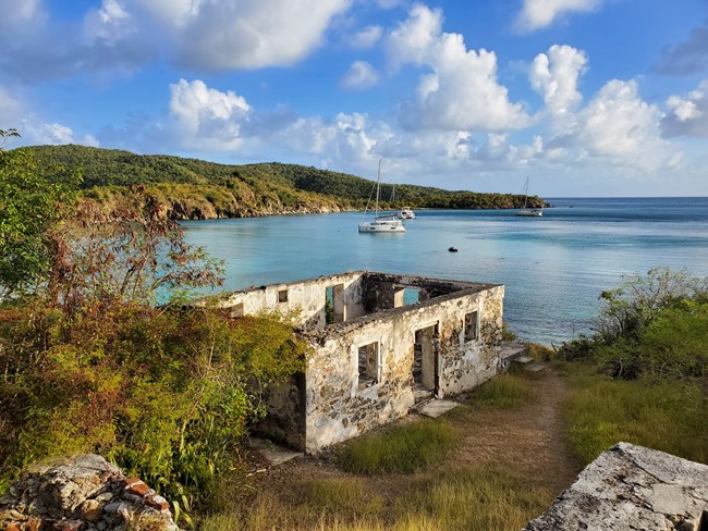 The ruins of a Danish sugar mill stand at the west end of Little Lameshur Bay Beach as its blue waters stretch off into the distance with the rolling green hills of Yawzi Point in the background.