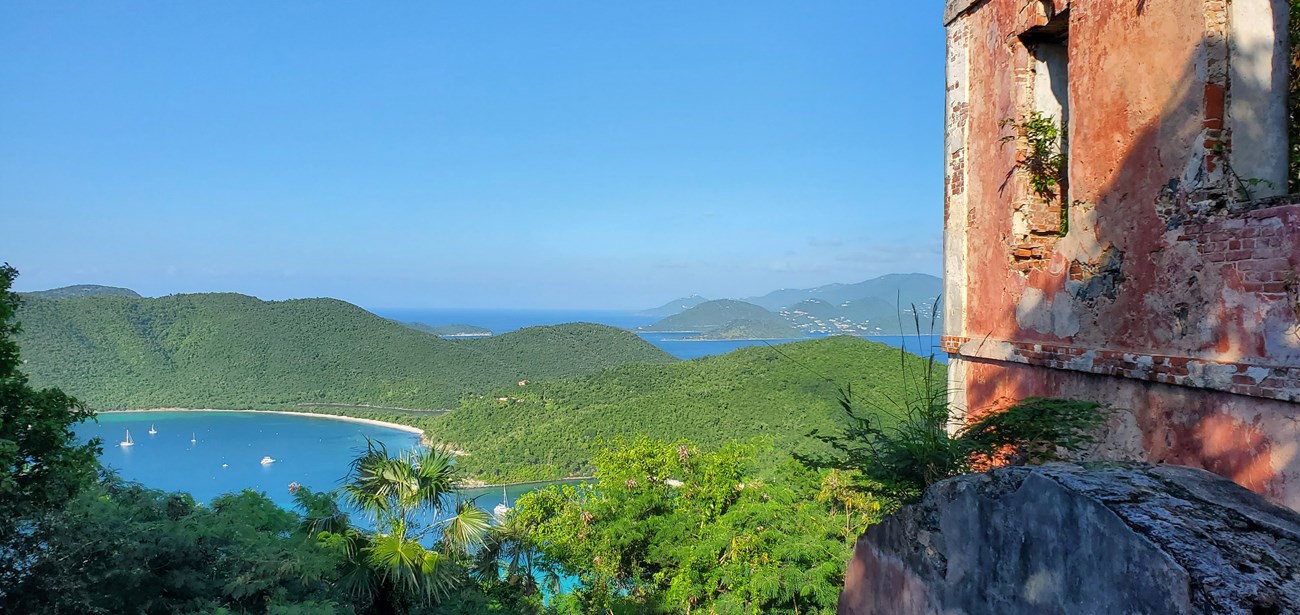 The America Hill ruins on Cinnamon Bay Trail are pictured alongside a panoramic view of the blue water of Francis and Maho bays, the green hillsides of St. John, and the British Virgin Islands in the distance.