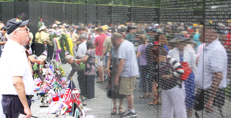 A man looks at the Vietnam Veterans Memorial on Memorial Day 2013. The wall has a large collection of flags, flowers, and memorabilia at its base, and many people's images are reflected in the wall. A man looks at the Vietnam Veterans Memorial on Memorial Day 2013. The wall has a large collection of flags, flowers, and memorabilia at its base, and many people's images are reflected in the wall.