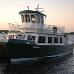 Voyageur Tour Boat Sunset on the lake lights up a 3 tiered boat with white on the upper decks and green on the lower.