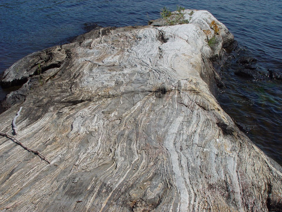 A rock outcrop in a lake, showing layers of dark and light colors.