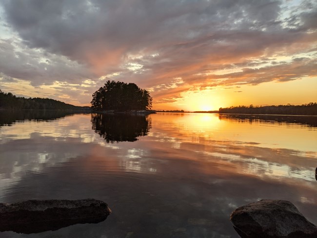 Sunset with clouds over a landscape of islands and water. Clouds and islands are reflected in the still water.