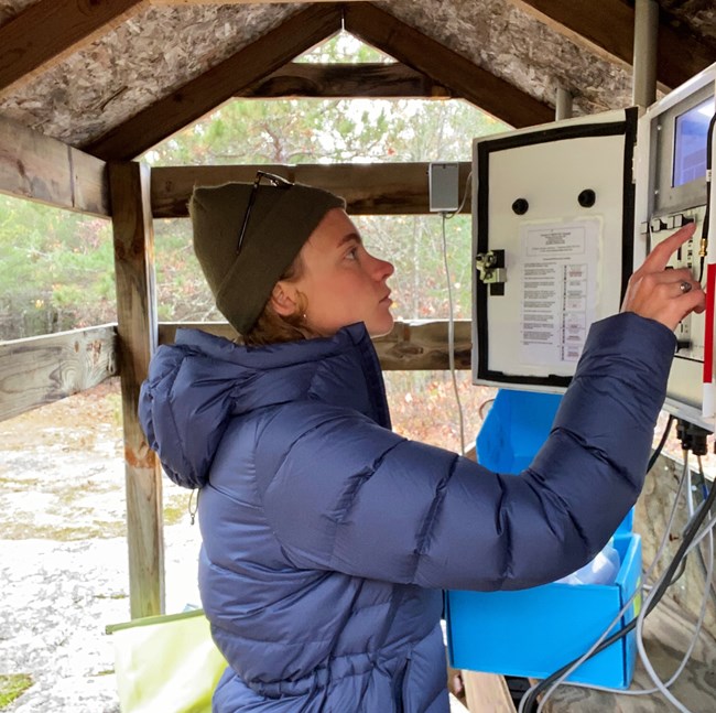 Standing in front of white air quality modules under a wooden structure, a technician uses a touch screen to access data.