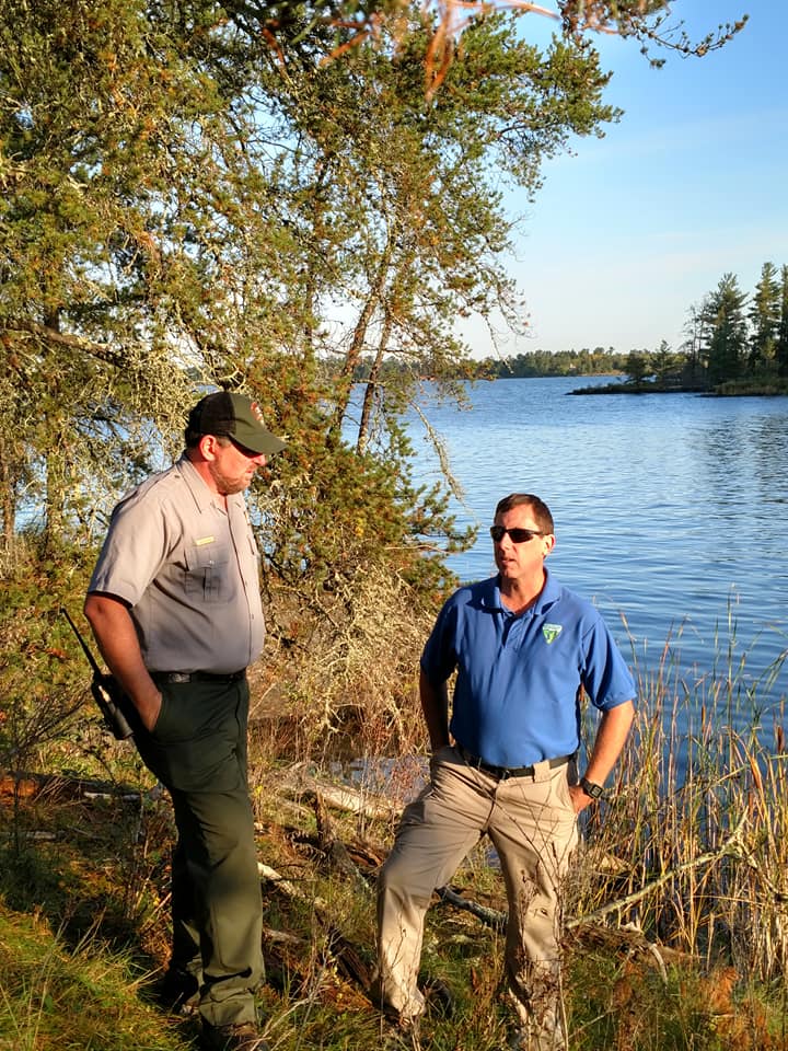Park Superintendent Bob DeGross and Bureau of Land Management (BLM) District Manager Dean Gettinger at a site visit in Voyageurs. Park Superintendent Bob DeGross and BLM District Manager Dean Gettinger stand on an island to be transferred into the park, with a scenic lakeshore in the background.