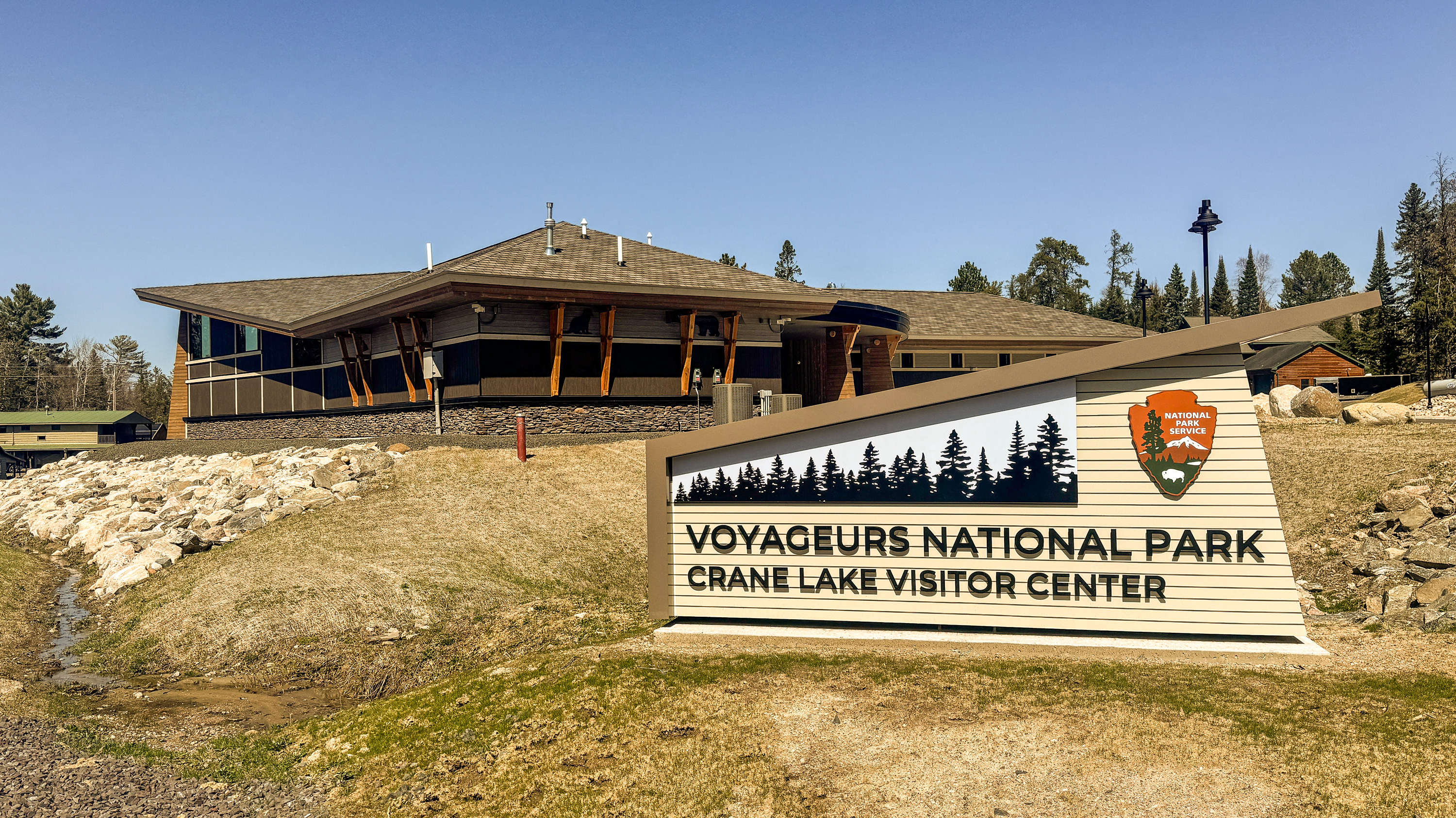 New Crane Lake Visitor Center Opening May 2025 New Crane Lake Visitor Center sign with building in the background on a sunny spring day with the ground still brown and no grass yet.