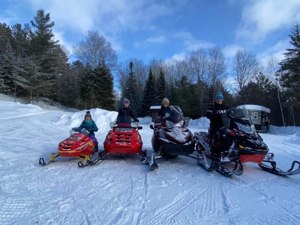 Ranger Chad and family on 4 snowmobiles in a clearing in the woods on a sunny winter day.