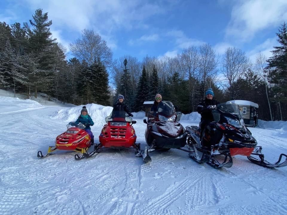 Ranger Chad and Family. Ranger Chad and family on 4 snowmobiles in a clearing in the woods on a sunny winter day.