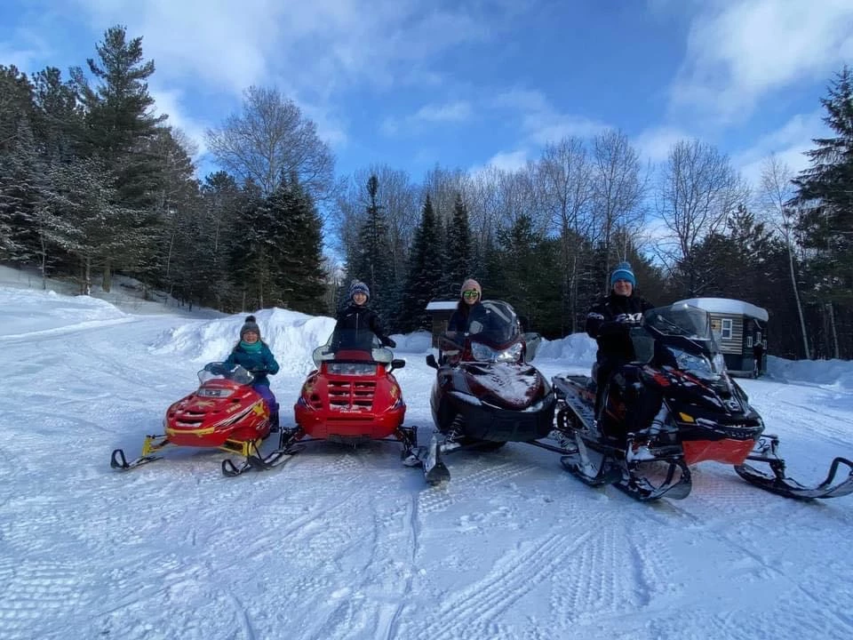 Ranger Chad and Family. Ranger Chad and family on 4 snowmobiles in a clearing in the woods on a sunny winter day.