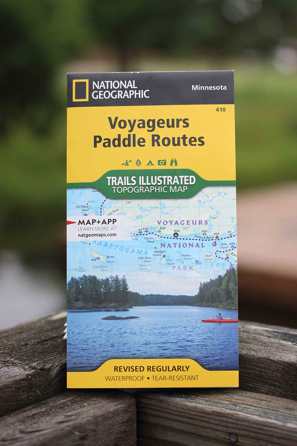 A folded map with a picture of a scenic lake on its cover lays on a wood surface.