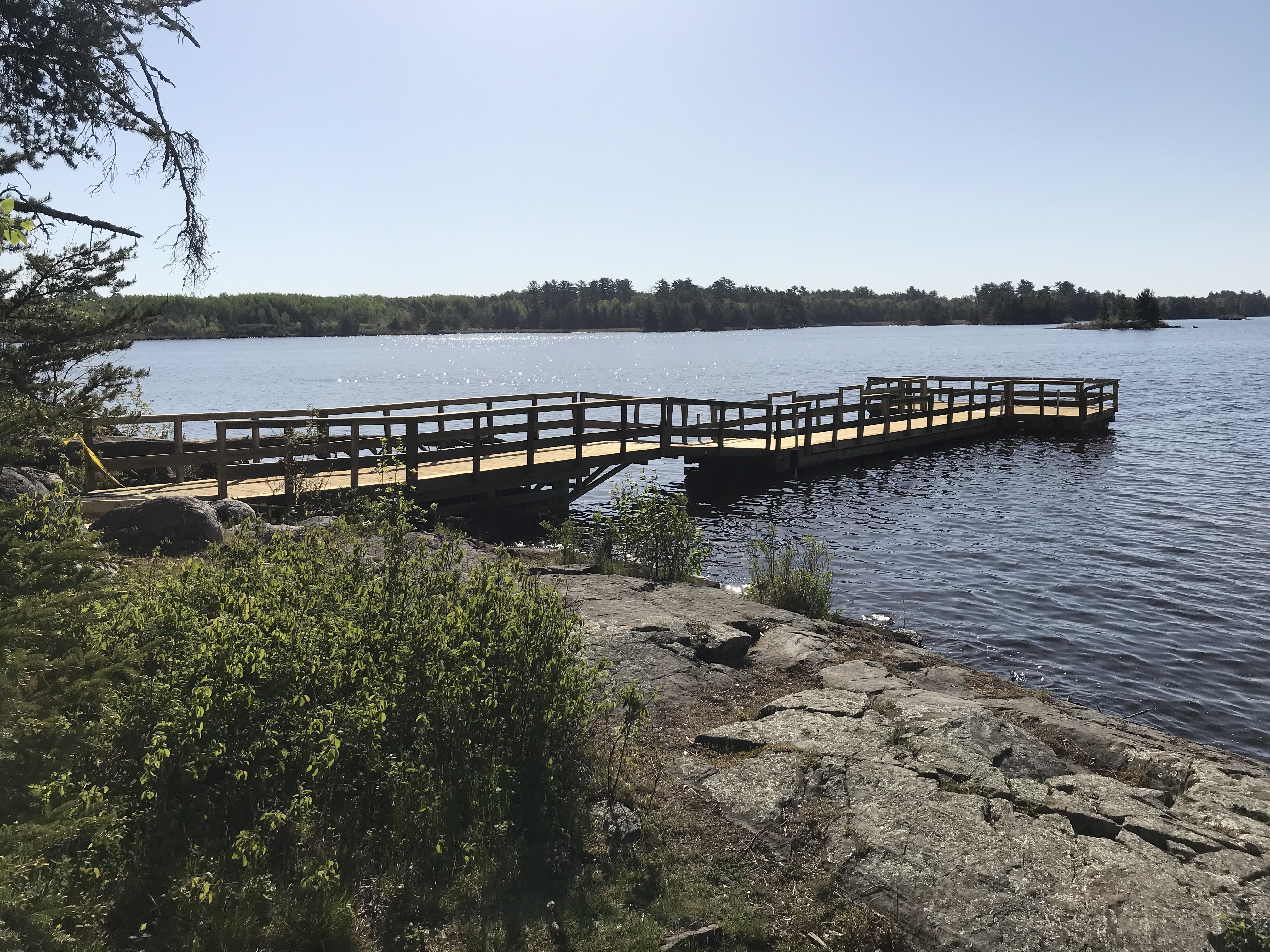 Wooden T shaped fishing pier extends from rocky shore into blue water