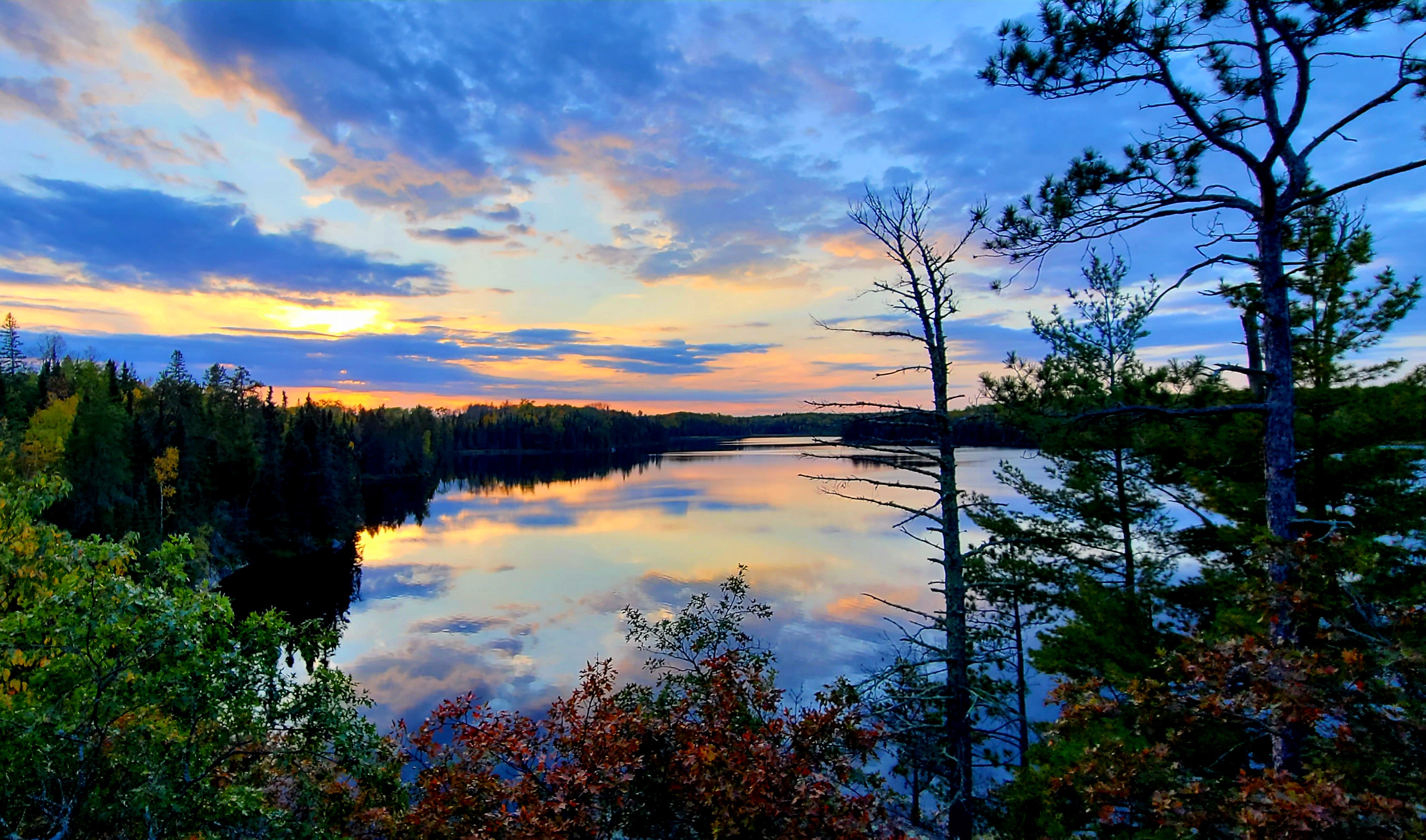Ek Lake Autumn Sunset. Photo credit: NPS/Mark Miller Orange, yellow, red sunset colors and clouds reflect upon the green and red foliage of the forest-lined shores of blue colored waters of Ek Lake.