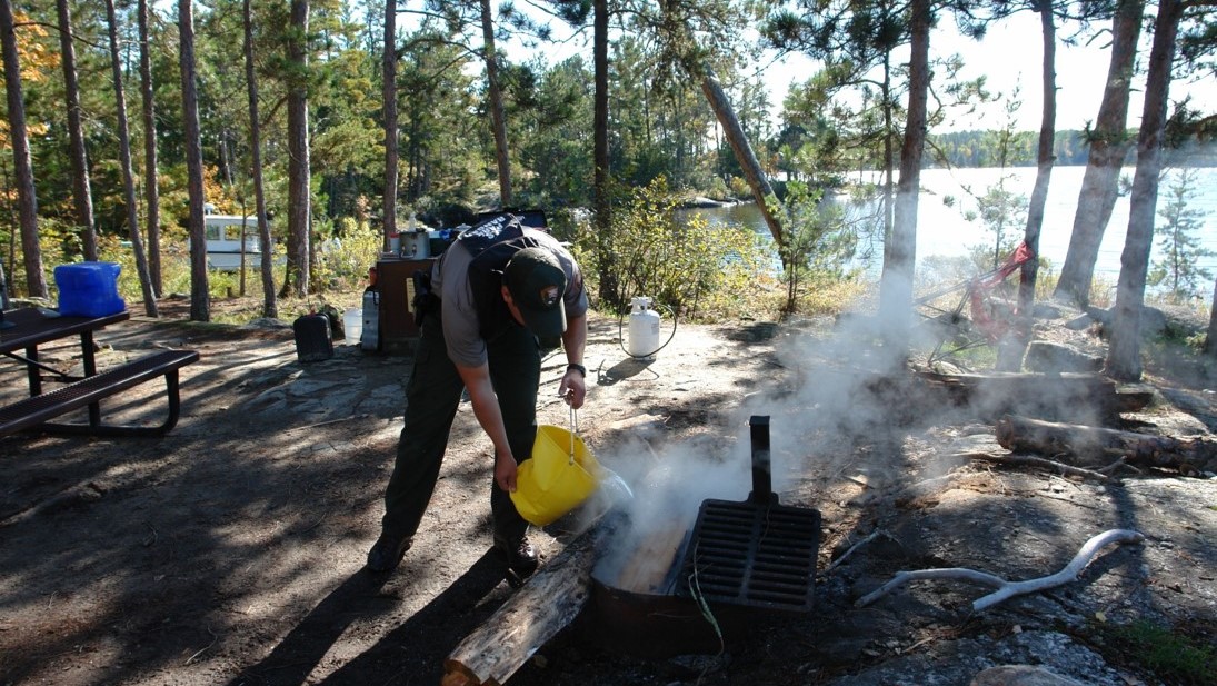 Putting out a campfire A Park Ranger uses a bucket of water to put out a campfire.