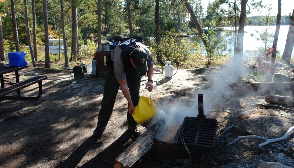 Please put out your campfire. Park Ranger douses a campfire with a bucket of water.