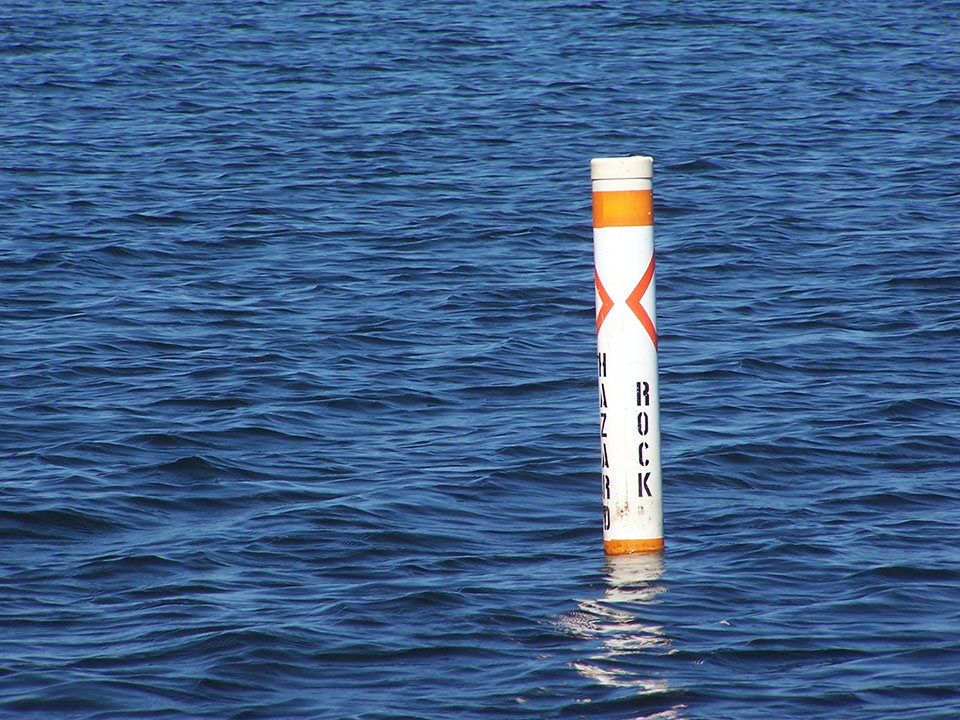 Rock markers can be seen across the lake during the summer marking numerous hazards. A white buoy with orange marking floats in the water with Rock written on it.