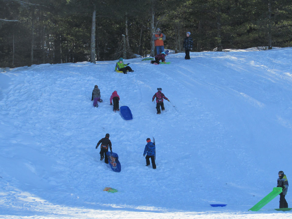 Sledding Hill on Kabetogama Many youth climbing up a snowhill, others getting ready to slide down.