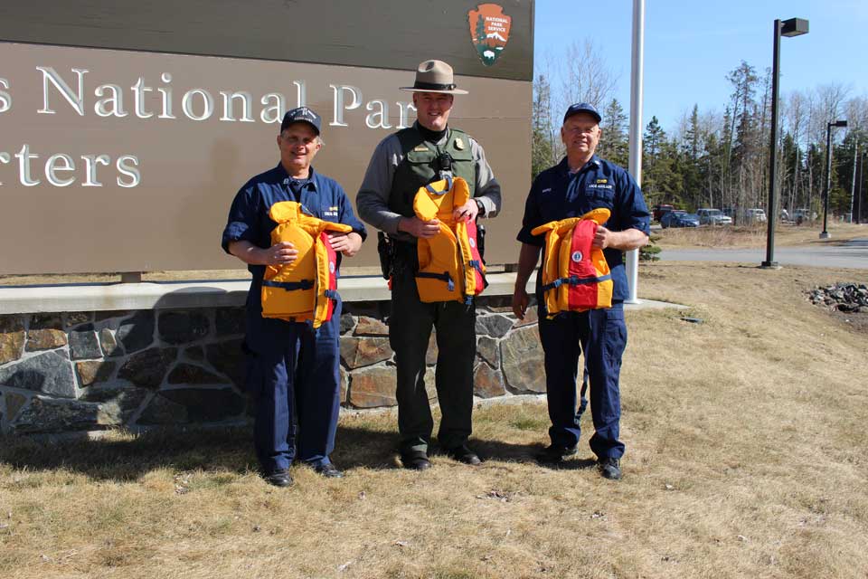 Three men standing in front of Voyageurs National Park sign each holding a youth life jacket.