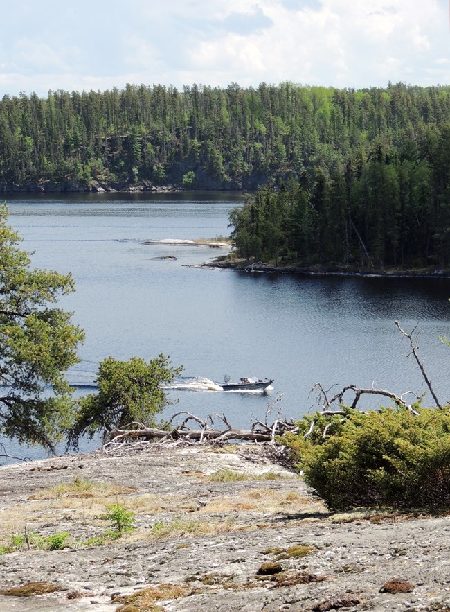 A motorboat planes quickly across the waters of a scenic lake, leaving a white line of waves in its wake.