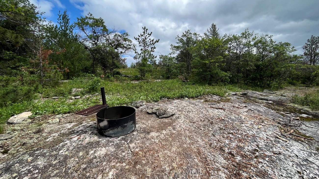 A fire ring sits on a granite outcrop surrounded by forest