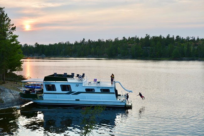 A family enjoys a houseboat moored to a forested shoreline