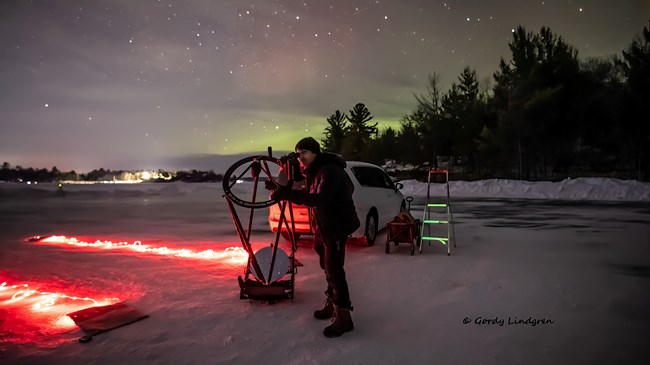 Photograph of person looking into telescope under a starry sky.