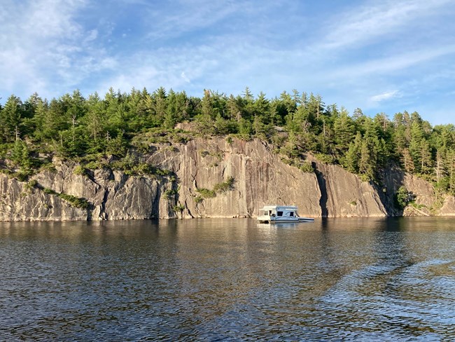 A houseboat drifts in front of the Grassy Bay Cliffs on Sand Point Lake